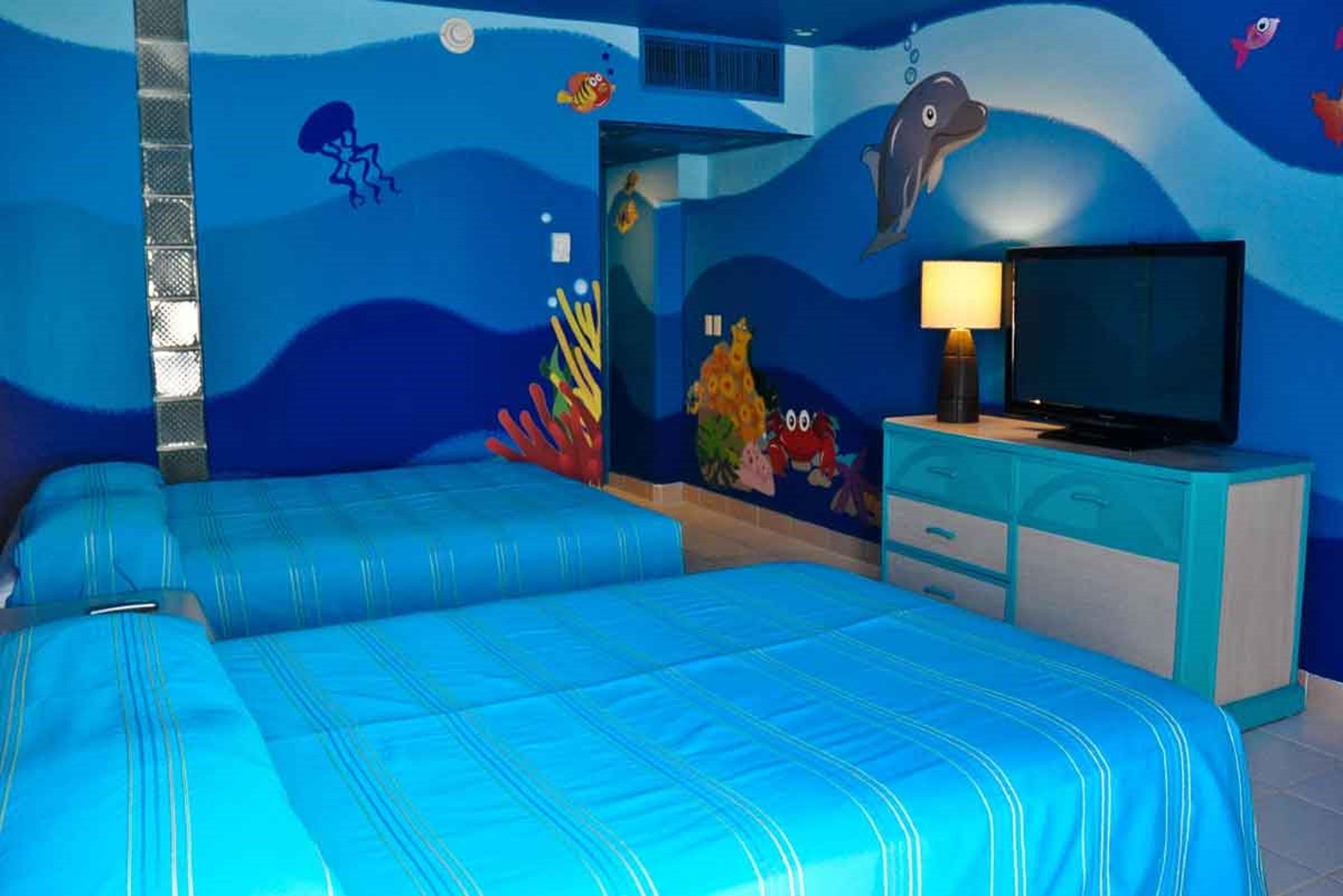 Отель Grand Oasis Palm Канкун Экстерьер фото The photo shows a brightly colored hotel room with a themed underwater design. The walls are painted in various shades of blue, resembling ocean water, and feature colorful sea creatures such as fish and a dolphin. There are two beds with blue stripe