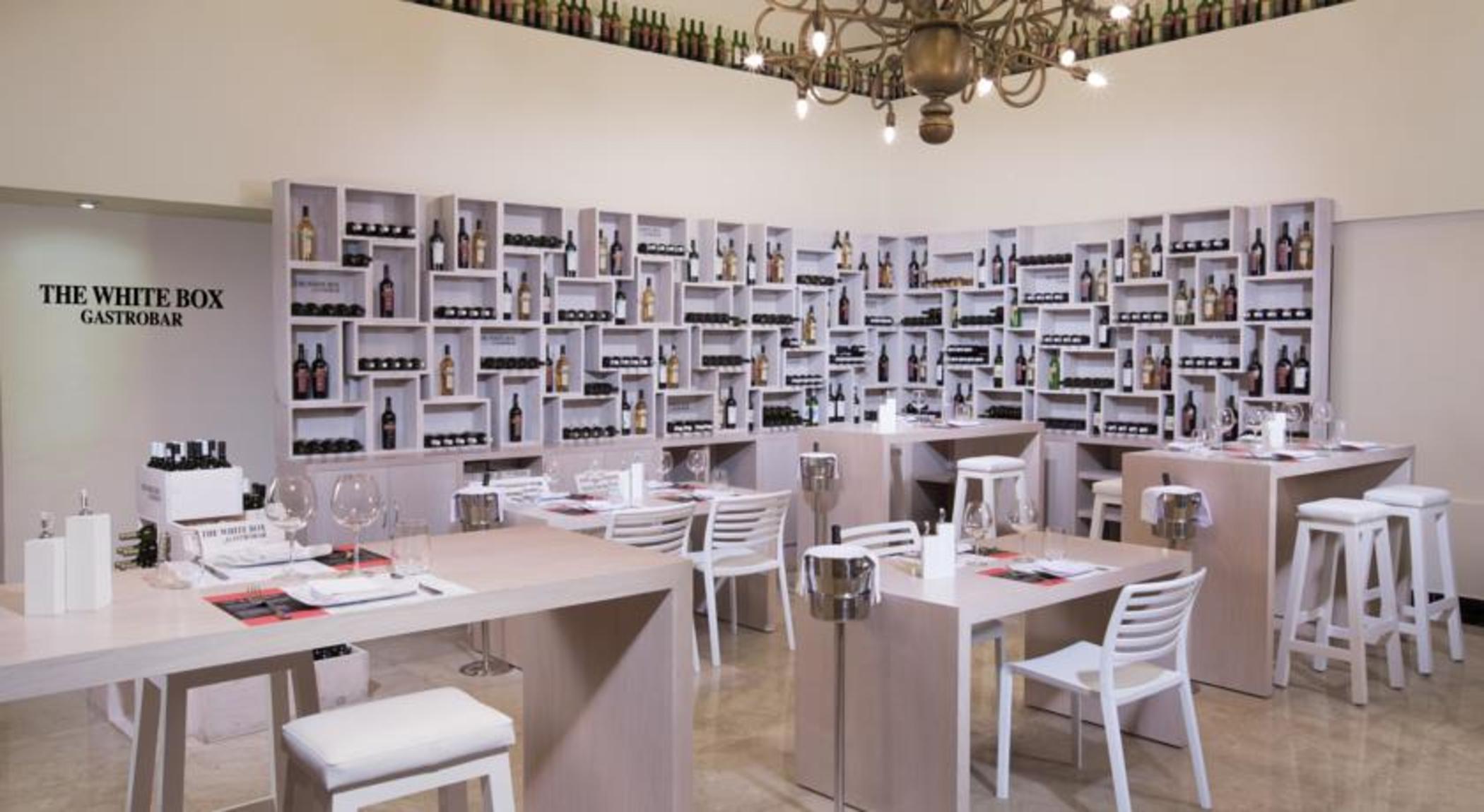 Отель Grand Oasis Palm Канкун Экстерьер фото The photo shows a modern restaurant interior. The walls are lined with shelves that display a variety of bottles, likely wine or spirits, creating a visually striking backdrop. The dining area features wooden tables and white chairs, offering a clean