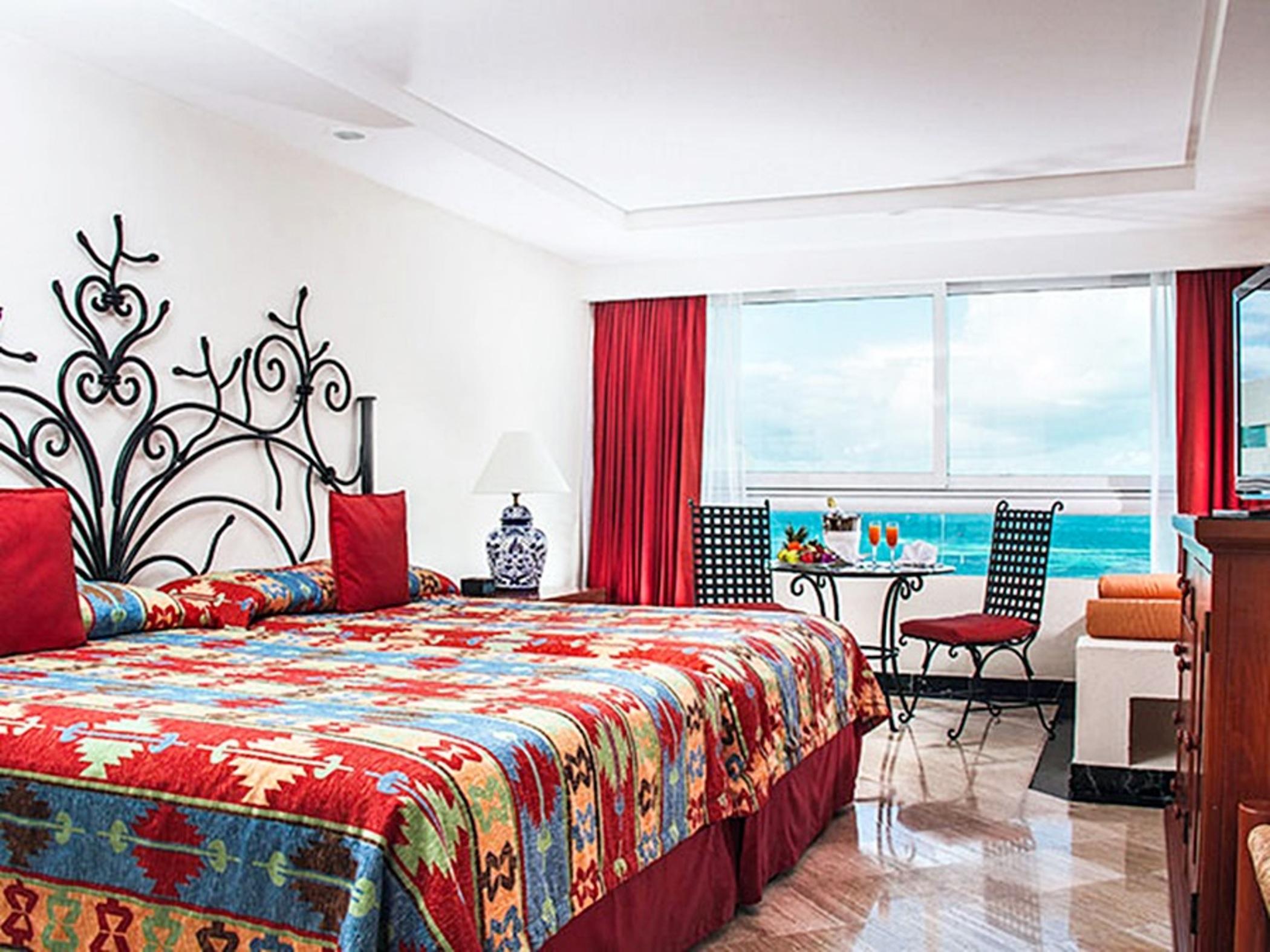 Отель Grand Oasis Palm Канкун Экстерьер фото The photo shows a well-decorated hotel room featuring two large beds with vibrant, patterned bedding. The headboards are stylishly designed, and the room has colorful accents like red curtains and cushions. A small table with chairs is positioned by 
