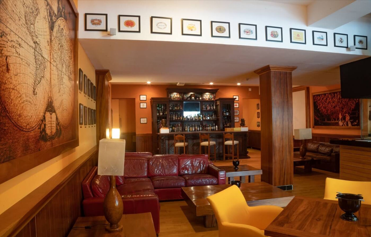 Отель Grand Oasis Palm Канкун Экстерьер фото The photo shows a cozy interior of a bar or lounge area. It features a comfortable setup with a deep red leather sofa and wooden tables. The walls are adorned with decorative artwork, including various framed pictures that add character to the space.